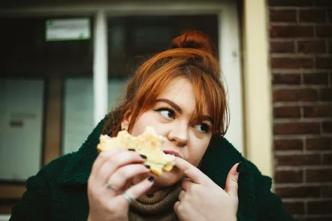 Frau sitzt gestresst vor einem Tisch voller Lebensmittel – Binge Eating Störung durch Stress