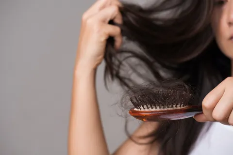 Frau betrachtet Haarausfall durch Stress – Haarbürste mit ausgefallenen Haaren