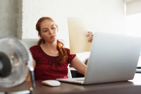 Schwitzender Büroangestellter am Schreibtisch leidet unter Hitzestress am Arbeitsplatz im Sommer
